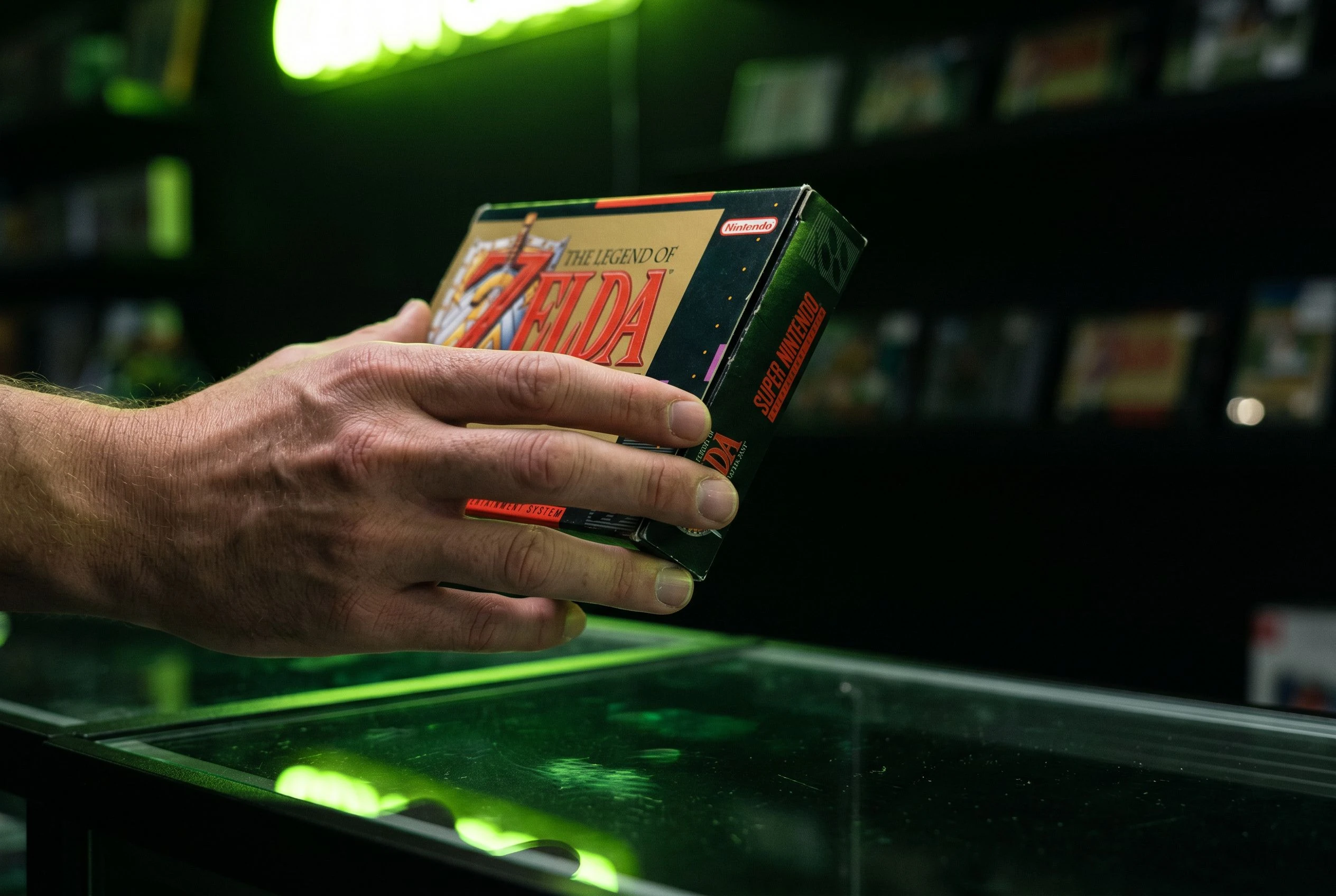 Eine Hand hält eine Spiele-Box über einer dunklen Ladentheke und inspiziert sie im neon-grünen Licht des Stores